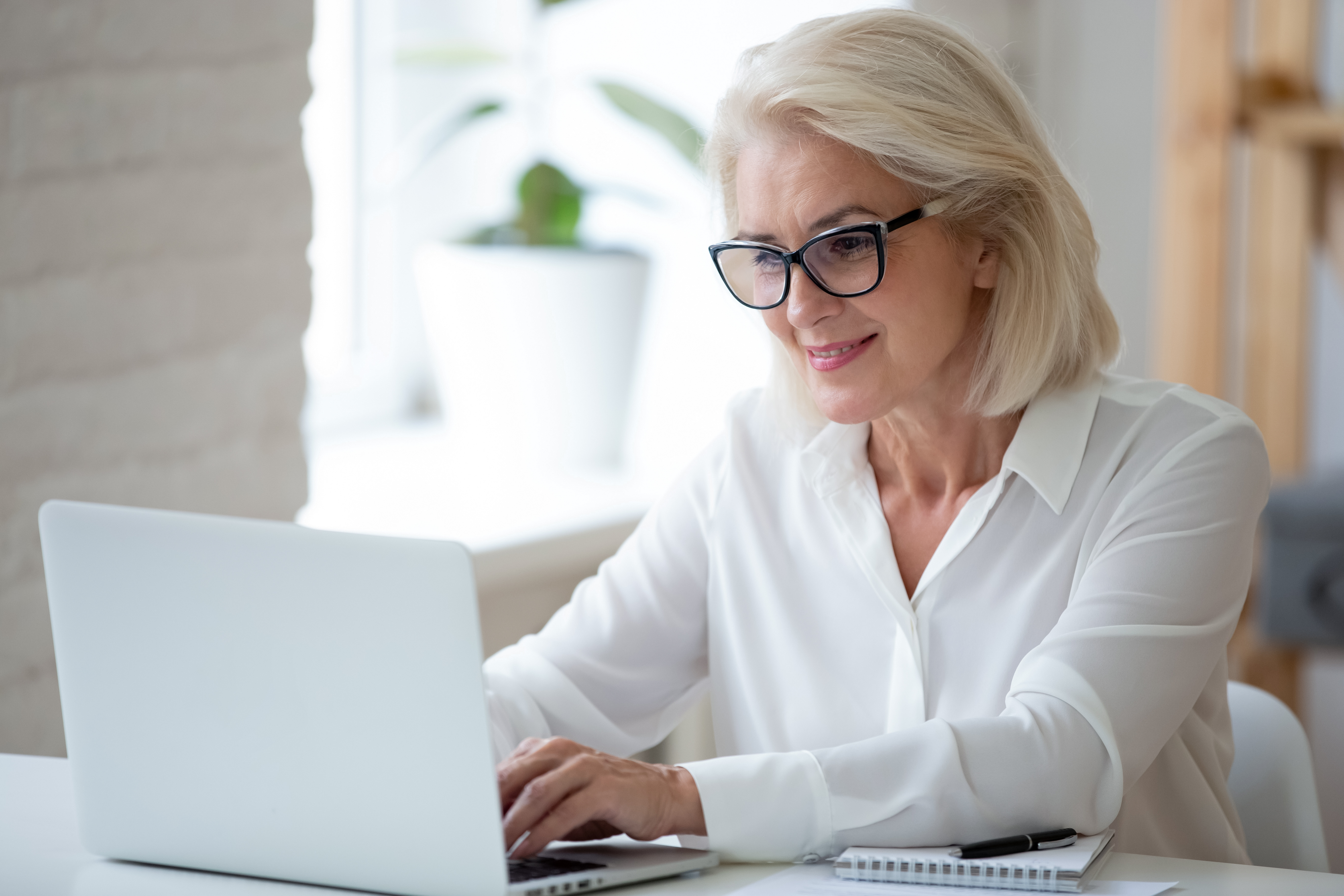 Focused middle-aged woman in glasses sit at desk typing working on laptop